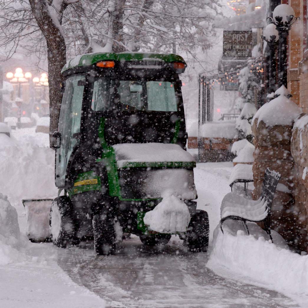 Pearl street being plowed by a small snowplow on a stormy winter day.