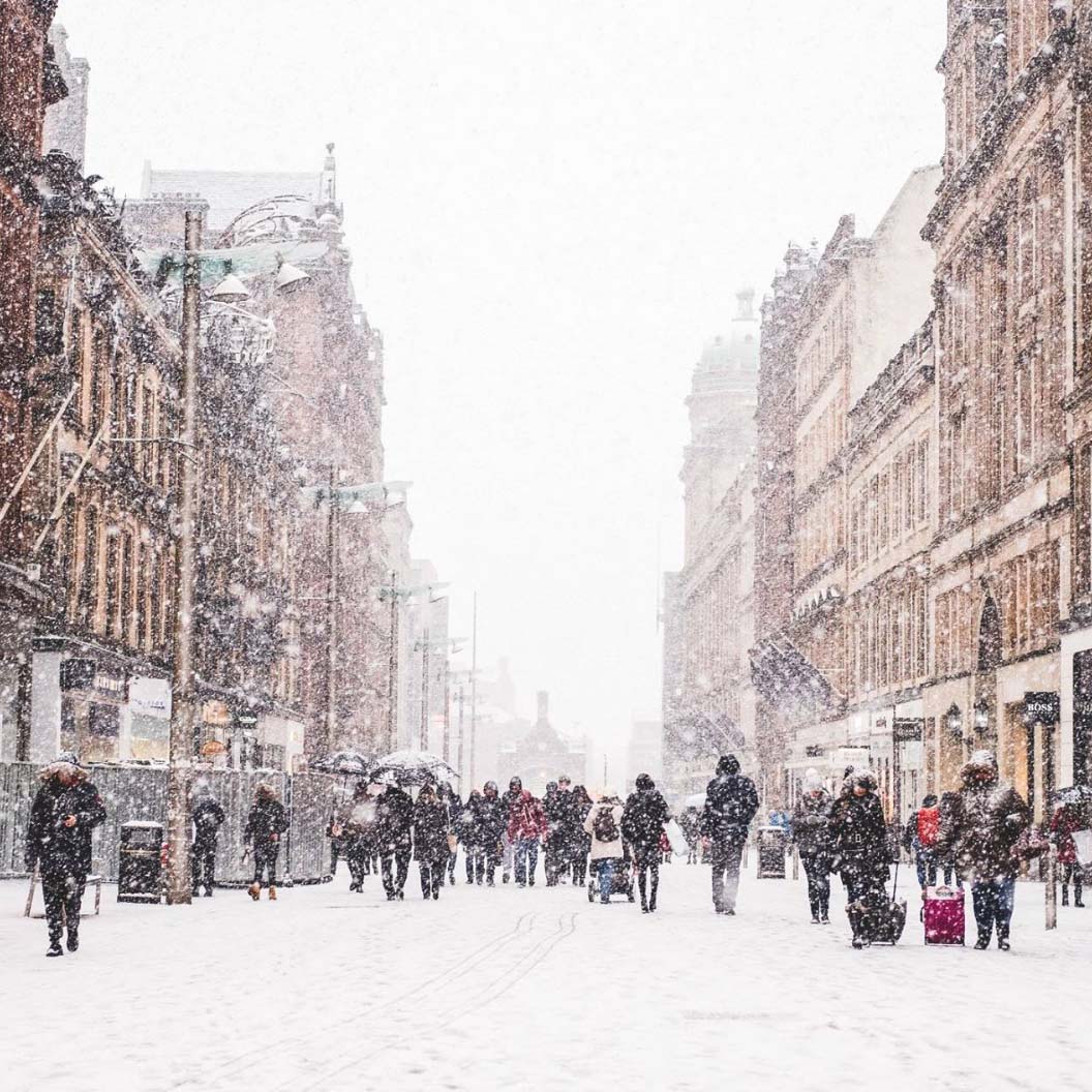 Les gens marchent lors dâ€™une journÃ©e dâ€™hiver orageuse. La rue est recouverte d'une fine couche de neige. Quelques personnes transportent des bagages au premier plan.