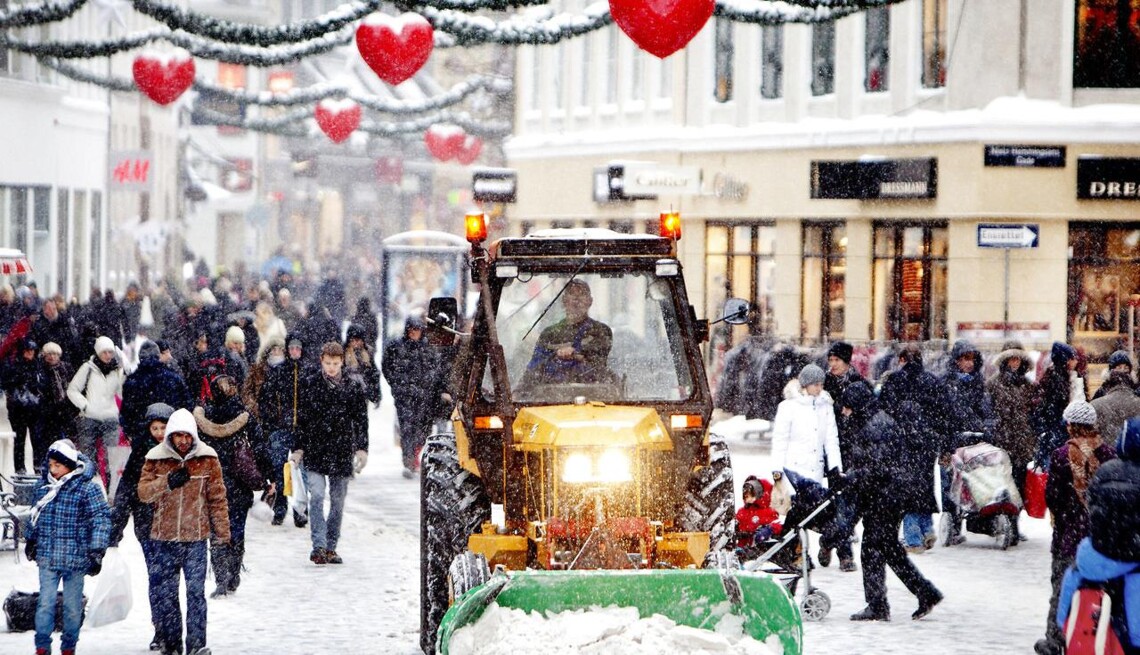 A snowy commercial street in Copenhagen being plowed with many people walking all around.